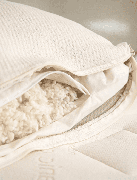 A close-up of a beige pillow with a zipper partially open, revealing shredded filling material inside.