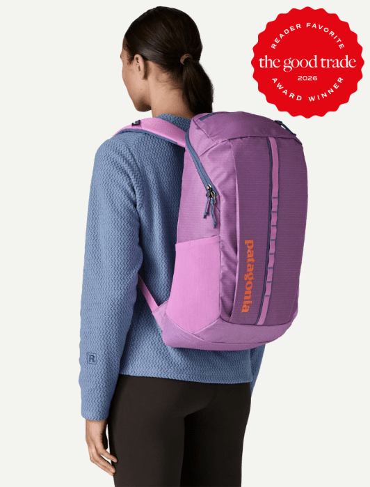 A woman wearing a blue textured sweater and black pants carries a large pink and purple Patagonia backpack. A red "The Good Trade Award Winner 2026" badge is in the corner.