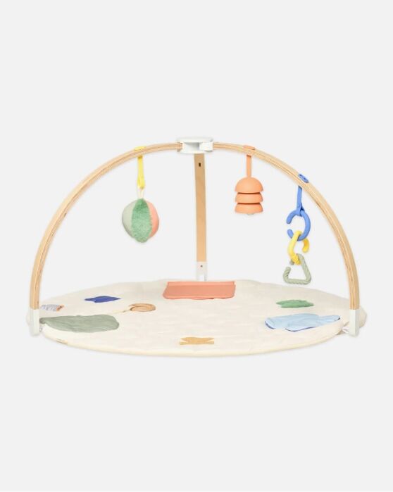 A baby play gym with a round padded mat, wooden arches, and hanging soft toys in pastel colors.