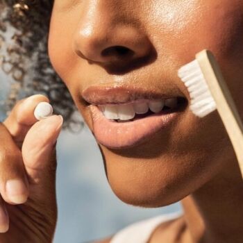 Close-up of a person holding a toothpaste tablet in one hand and a bamboo toothbrush in the other, about to brush their teeth.