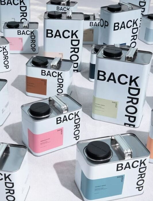 Several rectangular metal cans labeled "BACKDROP," each with different colored swatches and black caps, are arranged on a white surface.