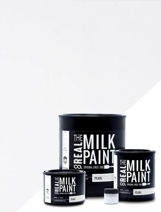 Three black containers of The Real Milk Paint Co. labeled "PEARL" are arranged on a white background, with a small open sample container in front.