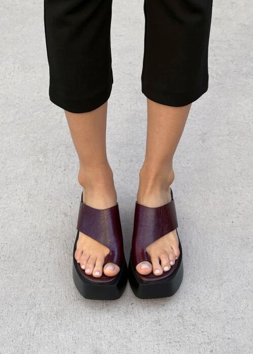 Person wearing black cropped pants and burgundy open-toe platform sandals standing on a light gray concrete surface.
