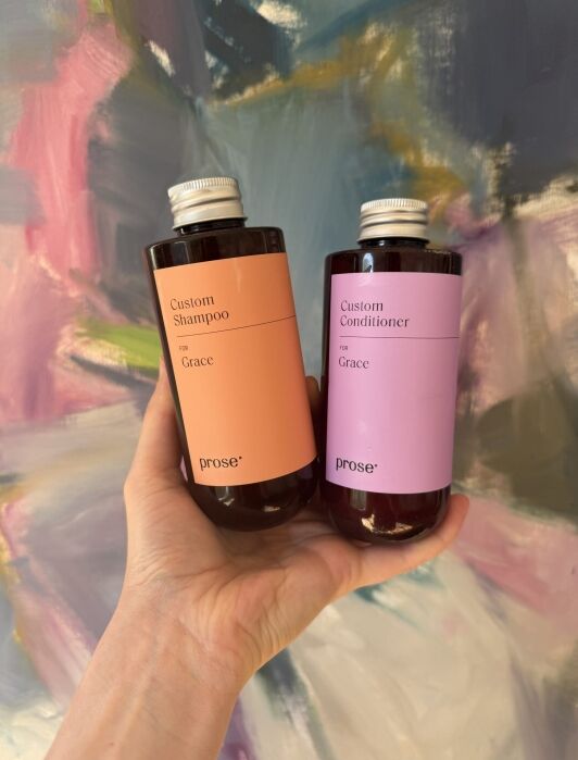 A hand holds two bottles labeled “Custom Shampoo for Grace” and “Custom Conditioner for Grace” against a colorful abstract background.
