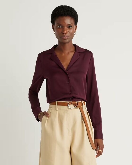 A person wearing a dark purple button-up blouse tucked into high-waisted beige trousers with a tan belt, standing against a plain light background.
