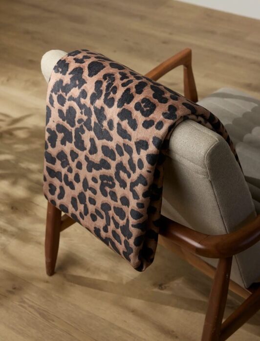 A brown and black leopard print blanket draped over the back of a light gray upholstered chair on a wooden floor.