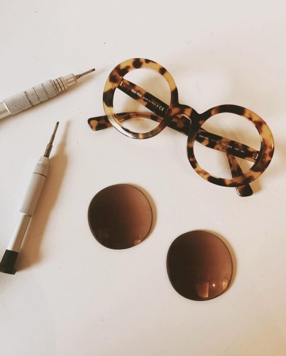 Round tortoiseshell eyeglass frames, two brown lenses, and two small screwdrivers are arranged on a white surface.
