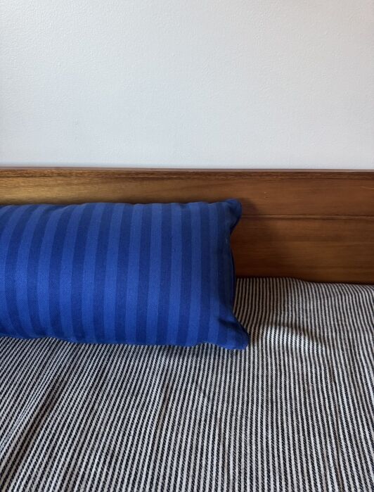 A blue striped pillow rests against a wooden headboard on a bed with a black-and-white striped blanket.