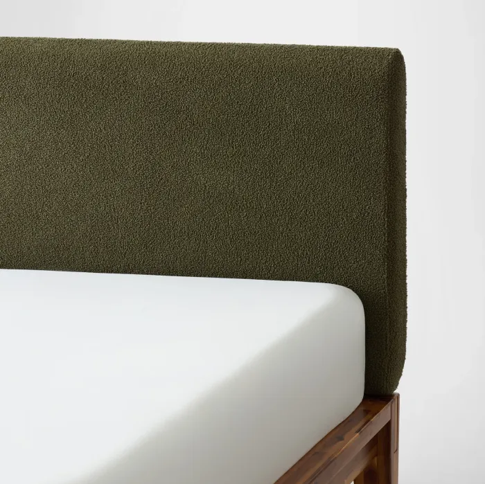 A bed with a white mattress, dark green textured headboard, and wooden frame against a plain light background.