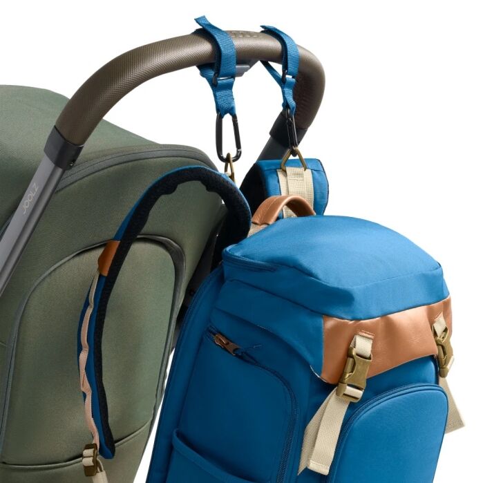 A blue and tan backpack is attached to a stroller handle using straps with metal hooks.