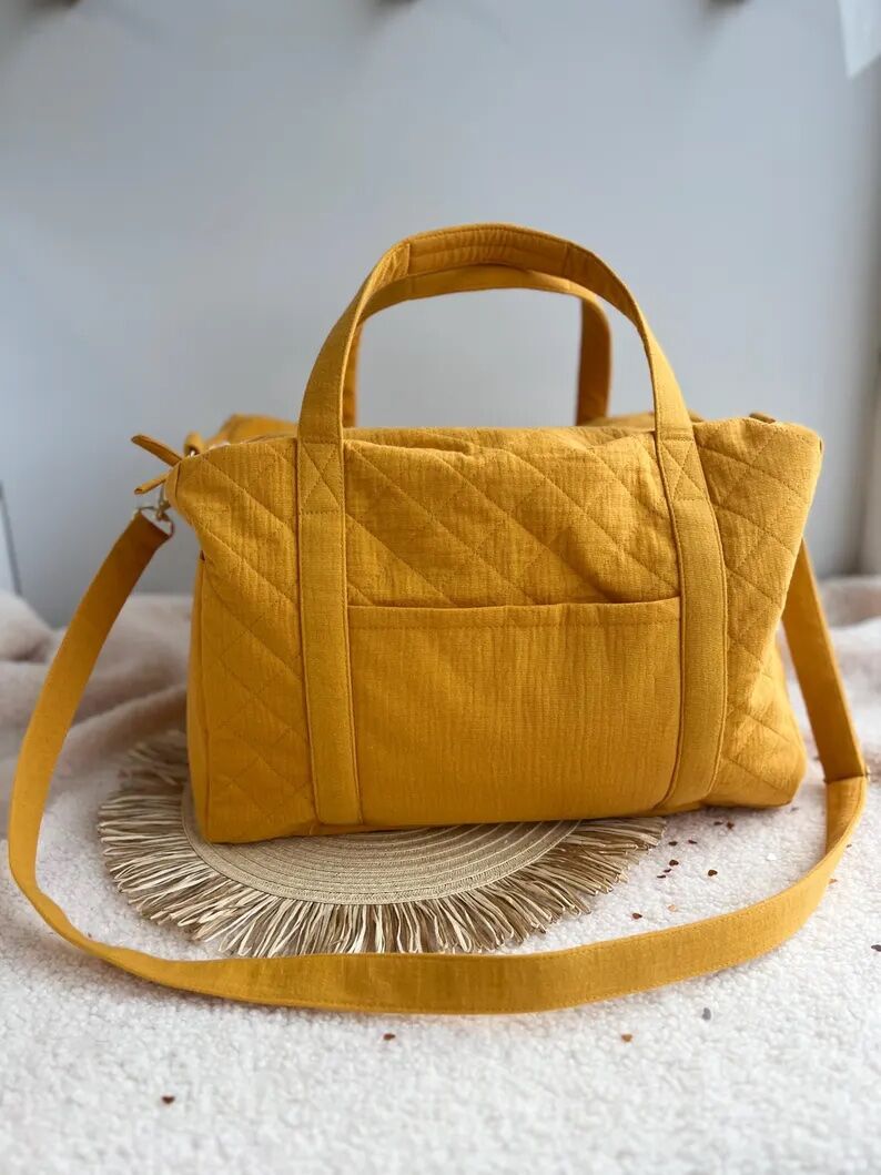 A mustard yellow quilted fabric handbag with double handles and a long shoulder strap, placed on a textured round placemat.