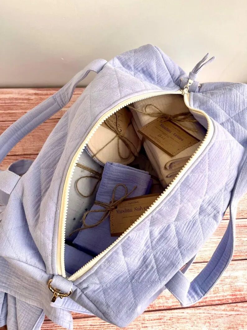 Open lavender quilted bag with several neatly wrapped fabric items inside, each tied with twine and brown tags, placed on a wooden surface against a neutral wall.