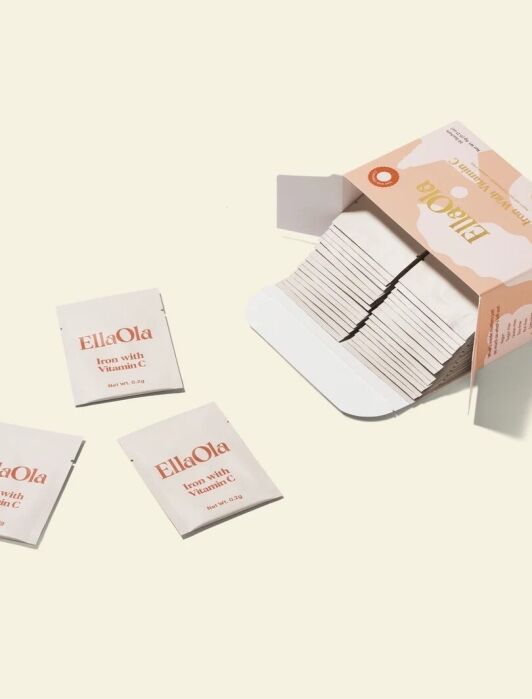 An open box of EllaOla individual sachets, with several sachets arranged outside the box on a light background.
