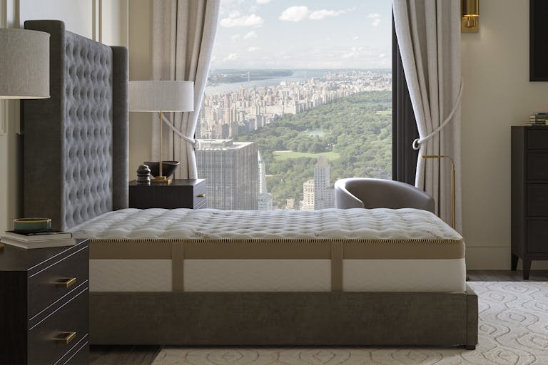 A modern bedroom with a large bed, two nightstands with lamps, and a window offering a high-rise view of Central Park and city buildings.