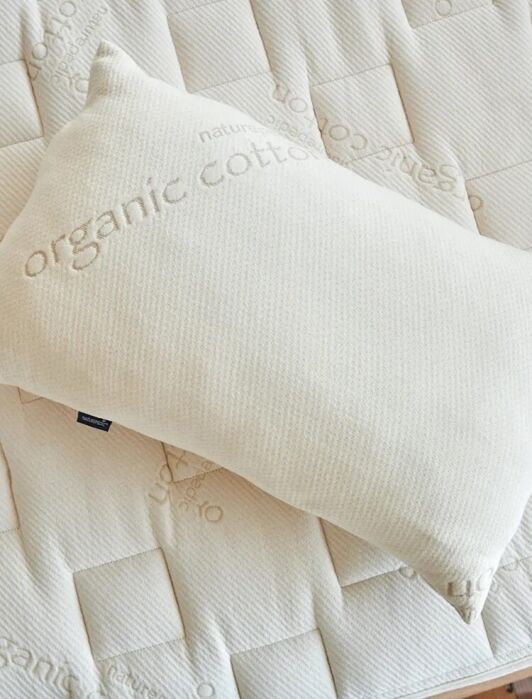 A rectangular pillow labeled "organic cotton" rests on a matching quilted mattress with the same "organic cotton" text pattern.