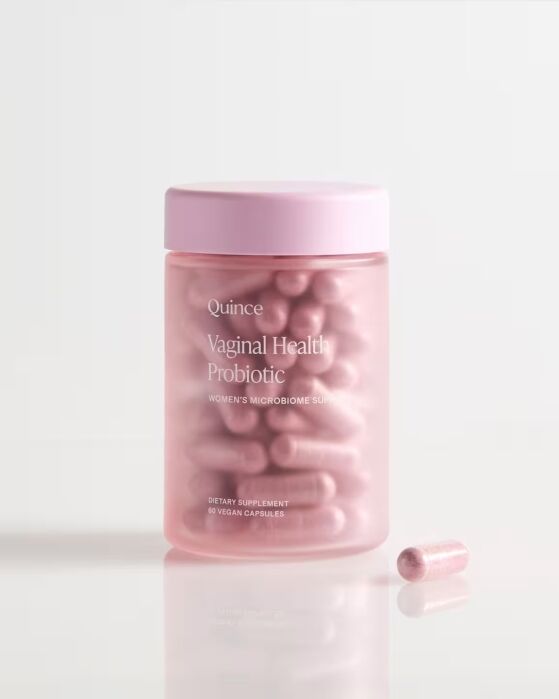 A clear jar labeled “Quince Vaginal Health Probiotic” contains pink capsules, with one capsule placed in front of the jar on a white surface.