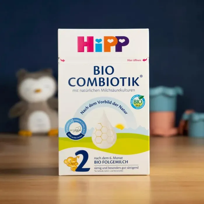 A box of HiPP Bio Combiotik 2 organic follow-on milk formula stands on a wooden surface with a blurred background.