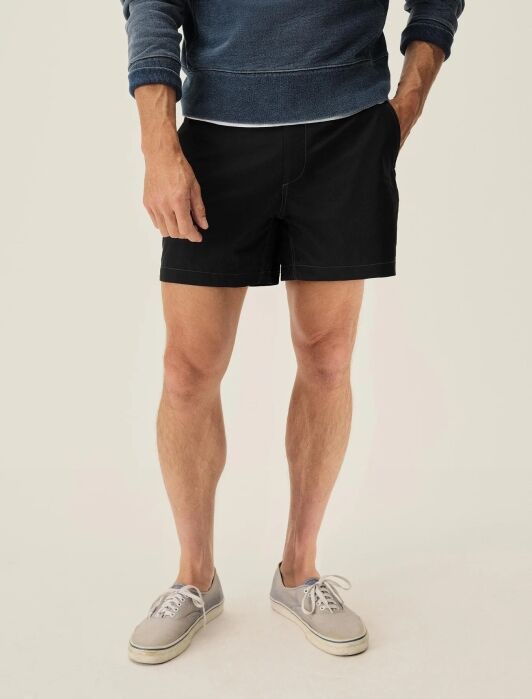 A person wearing a blue sweatshirt, black shorts, and gray canvas sneakers stands against a plain light background.