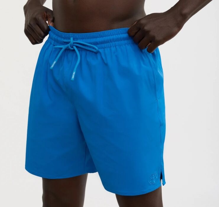 A person wearing bright blue swim trunks with a drawstring, standing against a plain background.