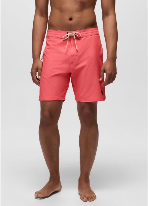 A person wearing coral pink swim trunks with a white drawstring, standing barefoot against a plain light gray background.
