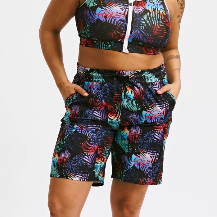 A person wearing a colorful tropical print crop top and matching shorts with hands in pockets, standing against a plain background.