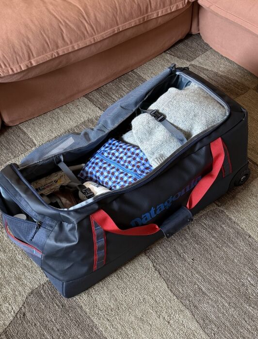 A black and red duffel bag on a carpeted floor, partially unzipped, showing folded clothes and a toiletry bag inside.