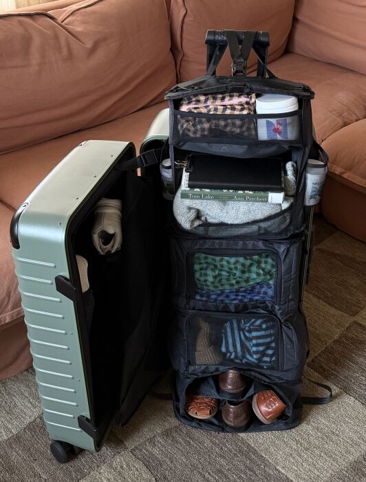 A packed suitcase sits open on the floor, revealing organized compartments with clothing, shoes, toiletries, and books.