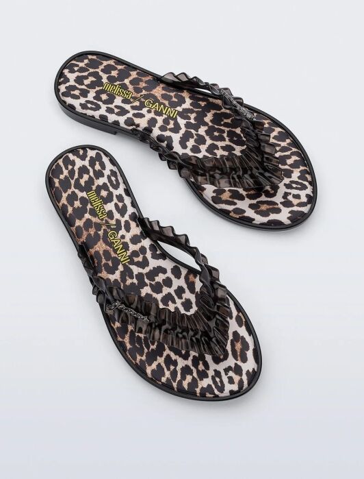 A pair of flip-flop sandals with a leopard print design and black ruffled straps, displayed on a plain white background.