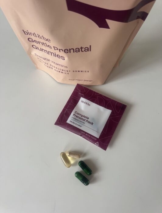 A packet of bird&be Gentle Prenatal Gummies, a sachet labeled "Complete Prenatal Pack," and four assorted prenatal vitamin capsules and tablets are arranged on a white surface.