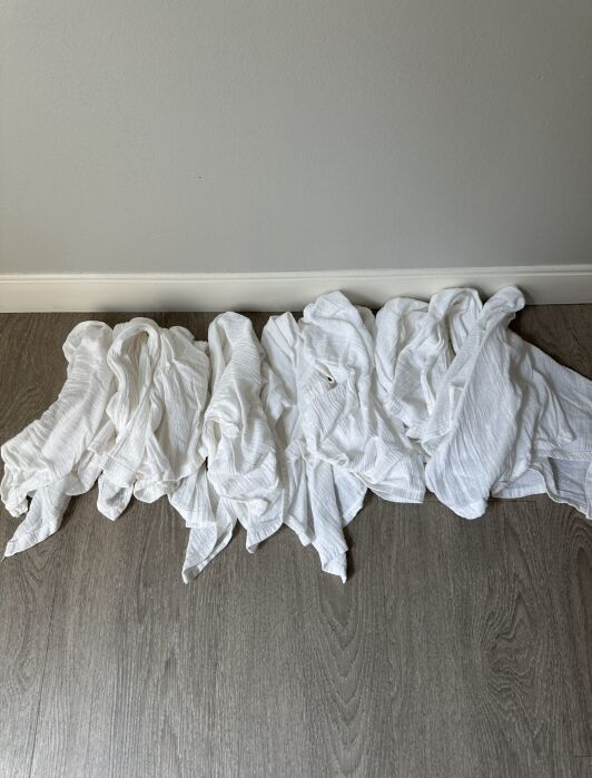A row of white, crumpled cloths lies on a light wood floor against a plain light gray wall with a white baseboard.