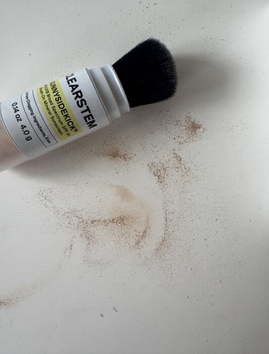 A makeup brush dispenser with loose powder scattered on a white surface.