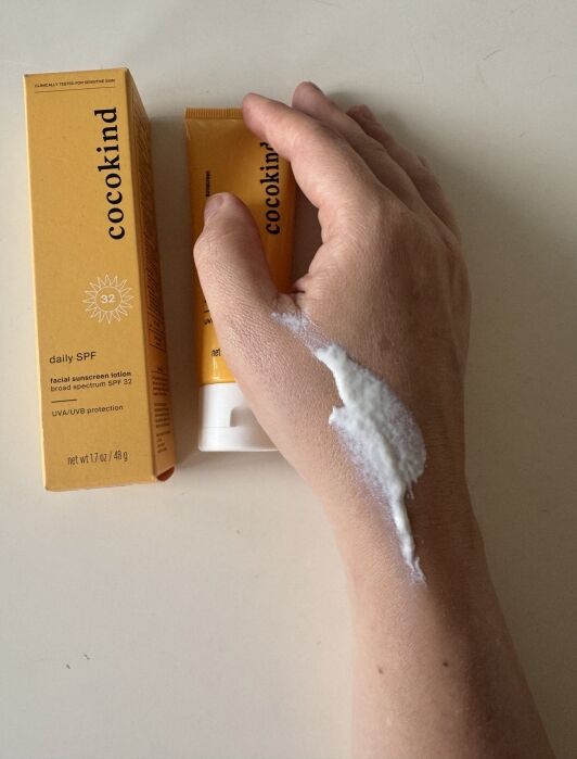 Cocokind SPF 32 facial sunscreen lotion is shown on a hand.