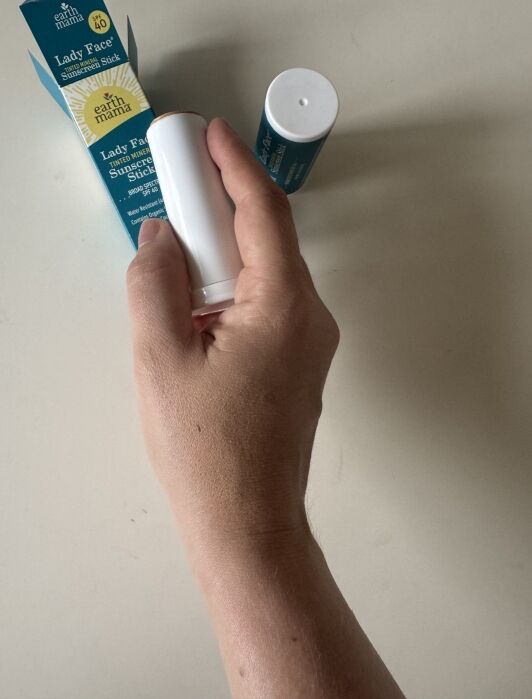 A hand holds a white tube labeled “Lady’s Face sunscreen stick” with its packaging and another stick on a light surface.