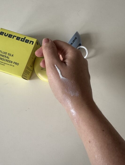 A hand with a streak of white sunscreen on the back is shown near a yellow Evereden sunscreen box and tube on a light surface.