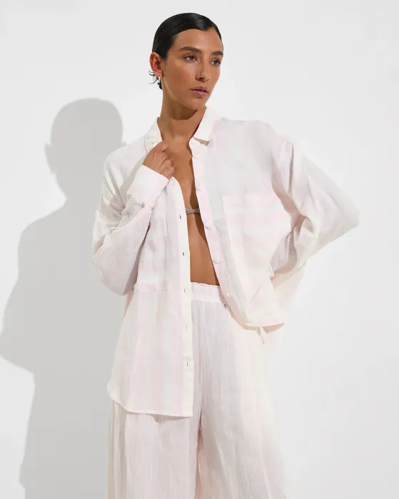Person wearing a loose, light-colored, button-up shirt and matching wide-leg pants, standing against a plain white background.