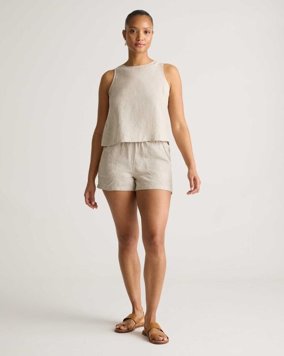 A woman stands facing forward wearing a sleeveless beige top, matching shorts, and brown sandals against a plain light background.