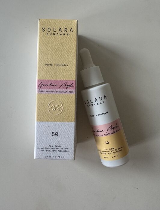 A Solara Suncare sunscreen milk bottle with dropper is placed next to its packaging box. Both are labeled "Guardian Angel" and have SPF 50 printed on them.