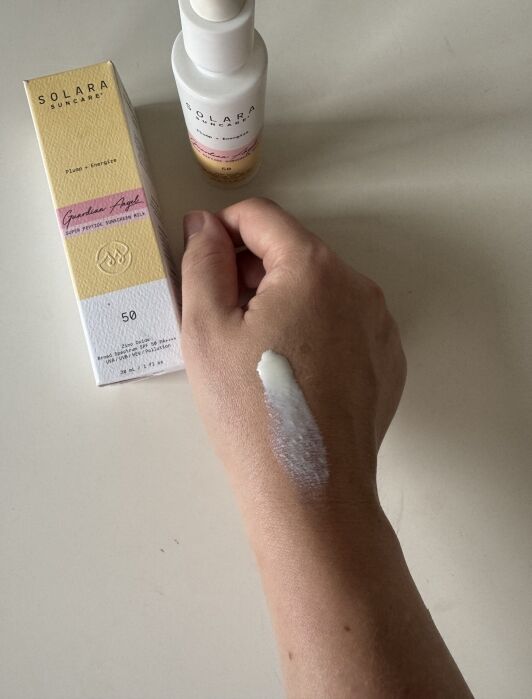 A hand with sunscreen lotion applied on the back is next to a Solara Suncare box and bottle of sunscreen on a white surface.