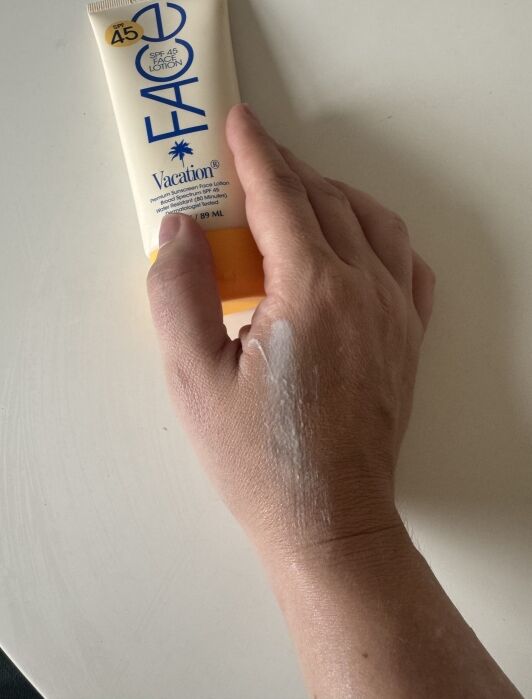 A hand with sunscreen lotion partially applied is shown next to a tube labeled "Vacation SPF 45 Face Sunscreen Lotion.