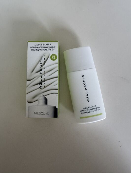 A bottle of Well People Daycleamer mineral sunscreen serum SPF 34 is shown next to its packaging on a white surface.