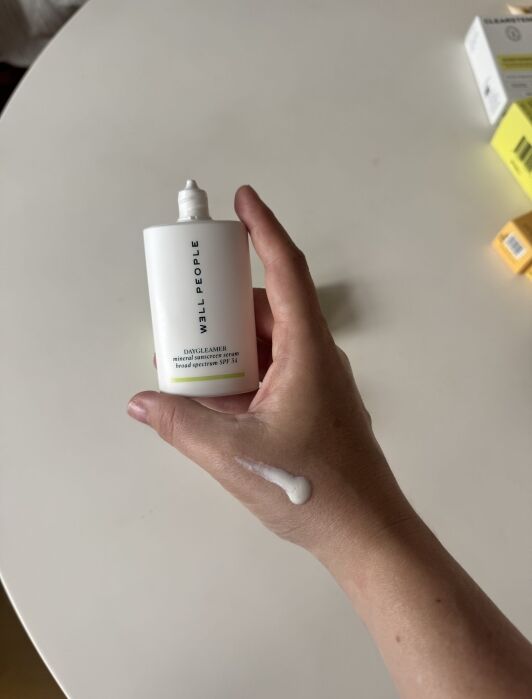 A hand holding a Milk People Daydreamer sunscreen bottle, with a small amount of sunscreen spread on the back of the hand.
