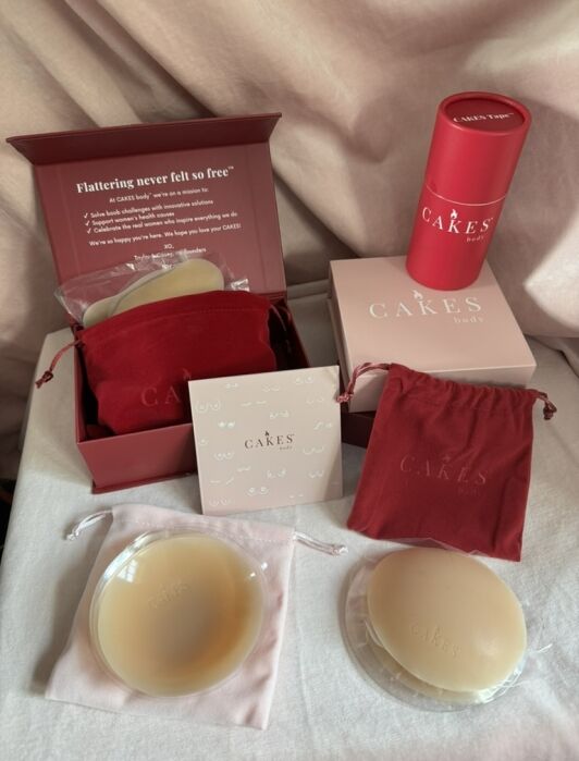 Two pairs of silicone nipple covers in pouches are displayed with pink and red CAKES Body branded boxes, a card, and a cylindrical container on a white surface.