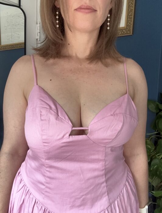 Woman in a sleeveless, light pink dress with spaghetti straps, standing indoors. The photo is cropped from shoulders to waist.