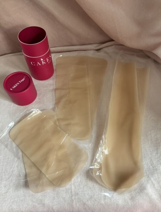 Two pink cylindrical containers labeled "CAKES" next to four beige silicone pads in clear plastic packaging on a light fabric surface.