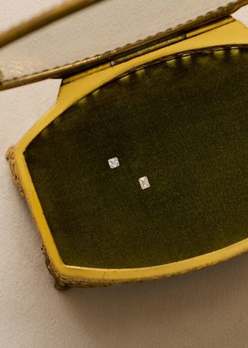 Two rectangular diamond stud earrings are displayed inside an open, olive green velvet jewelry box with a yellow exterior.