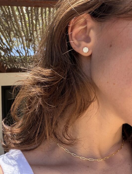 A close-up of a woman's ear with a round stud earring and part of her neck showing a gold chain necklace.