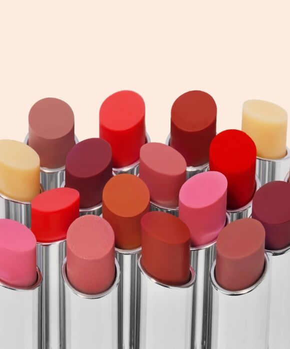 A variety of lipstick tubes in different shades of red, pink, orange, and nude are arranged closely together against a light background.