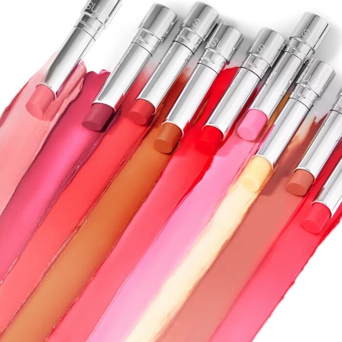 Ten silver tubes of lipstick in various shades lay side by side, with each lipstick color swiped directly beneath its corresponding tube.