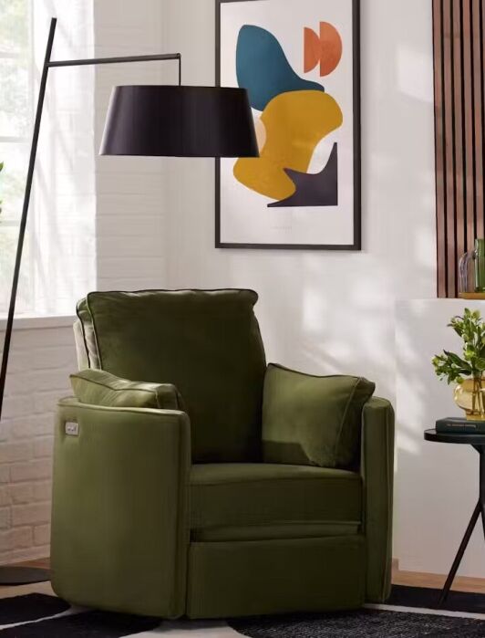 Green armchair beside a black floor lamp, abstract wall art, small side table with a plant, and a basket with a yellow blanket in a modern living room with natural light.