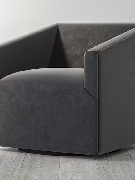 A modern, dark gray swivel armchair with angular armrests sits on a light wood floor against a plain white wall.
